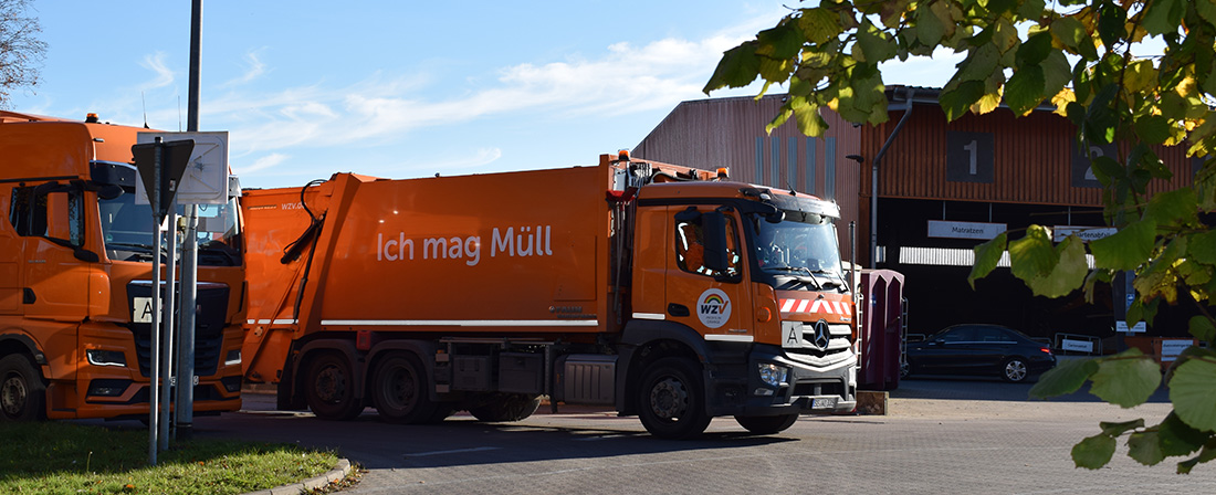 Ein oranger LKW der Abfallentsorgung fährt vom Recyclinghof los
